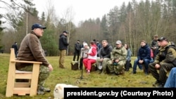 Аляксандар Лукашэнка на сустрэчы з праўладнымі журналістамі. Лукашэнка ў драўляным крэсьле, а журналісты — на калодках